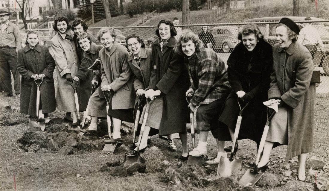 ten women standing in line with shovels in ground